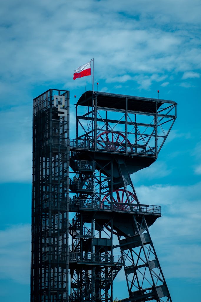 A dramatic industrial tower showcasing the Polish flag in Katowice, Poland against a blue sky.