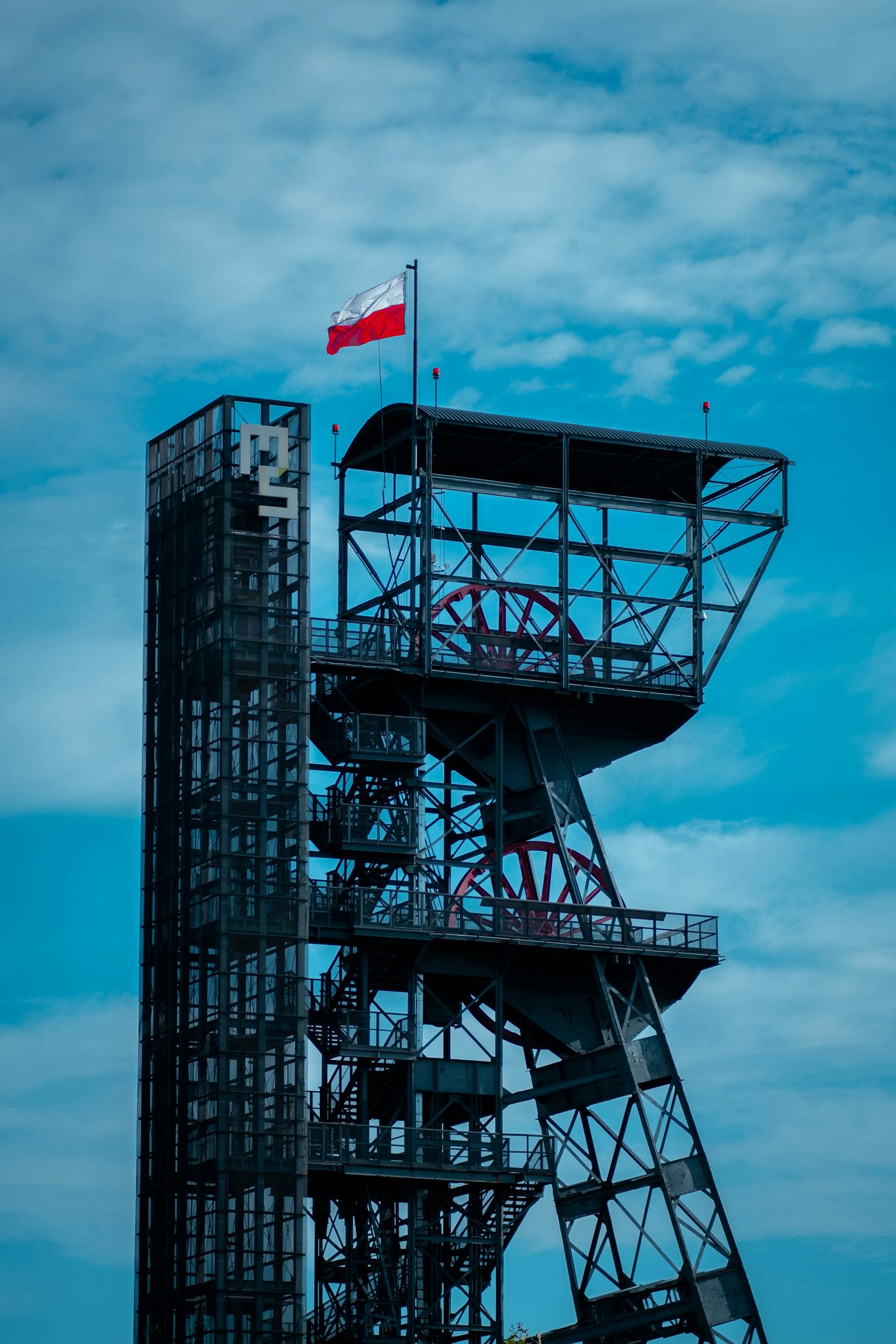 A dramatic industrial tower showcasing the Polish flag in Katowice, Poland against a blue sky.